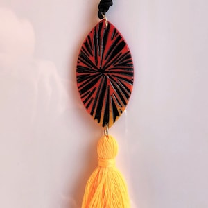 Peut inclure: Un collier avec un pendentif ovale rouge, jaune et noir avec un motif géométrique et un pompon jaune.
