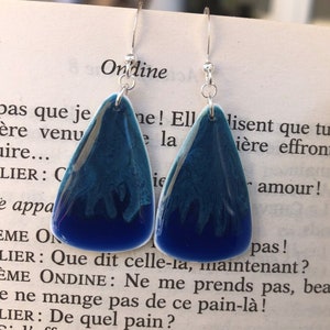 May include: A pair of teardrop-shaped earrings with a gradient of blue hues. The earrings have a glossy finish and silver-colored hooks. The text "Ondine" is visible in the background.
