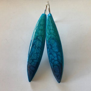 Puede incluir: Un par de pendientes en forma de lágrima de color azul turquesa y azul oscuro con ganchos plateados.