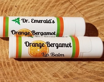 May include: Two white tubes of Dr. Emerald's Orange Bergamot Lip Balm. The tubes have green, orange, and white stripes with a picture of an orange slice on the front.