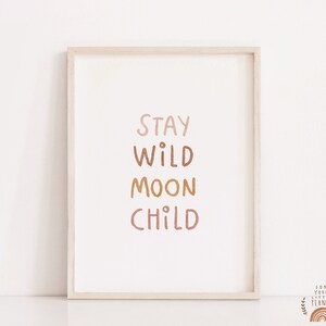 May include: A framed print with the text "Stay Wild Moon Child" in a gradient of brown, orange, and pink colors. The print is in a light wood frame.