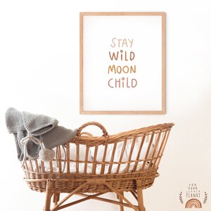 May include: A framed print with the text "Stay Wild Moon Child" in a light brown frame. The print is hanging on a white wall above a wicker bassinet.