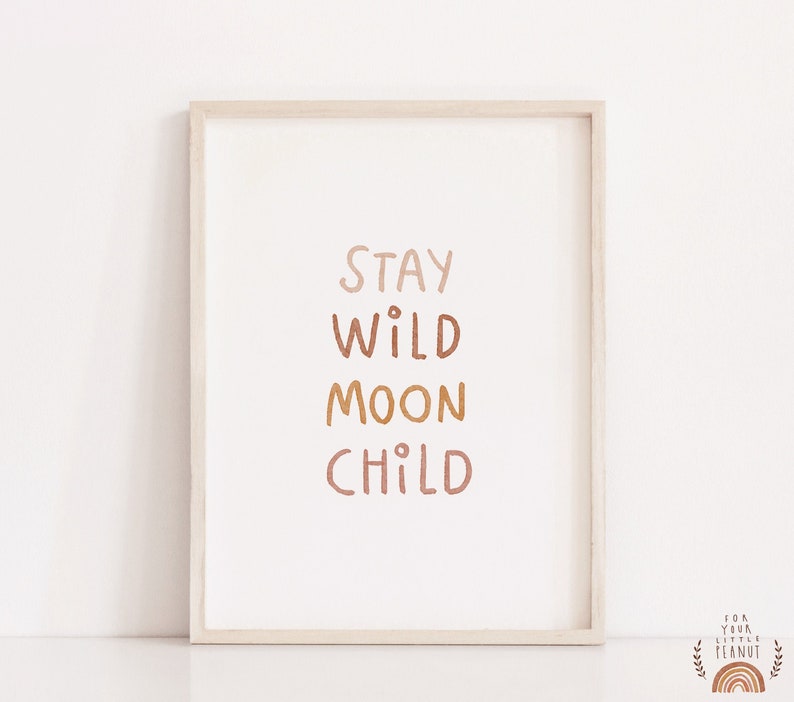 May include: A framed print with the text "Stay Wild Moon Child" in a gradient of brown, orange, and pink colors. The print is in a light wood frame.
