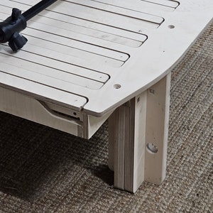 May include: A light-colored wooden bed frame with a slatted design. A black and silver tripod is resting on the bed frame. The bed frame is on a brown woven rug.
