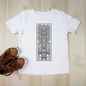 May include: A white t-shirt with a gray graphic print of a stylized figure. The figure is in a rectangular frame. Brown leather shoes with white soles are next to the shirt.