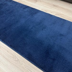 May include: A rectangular, navy blue rug with a soft, plush texture. The rug is placed on a light-colored wooden floor, creating a contrast between the dark blue and the light wood.