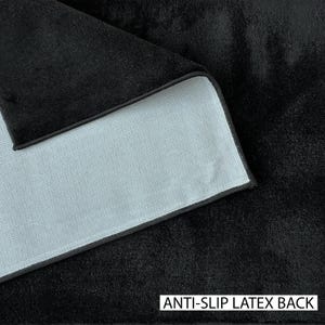 May include: Close-up of a black, textured fabric with a light gray backing. The edge of the fabric is visible, showing a black border. The text "ANTI-SLIP LATEX BACK" is printed in white at the bottom.