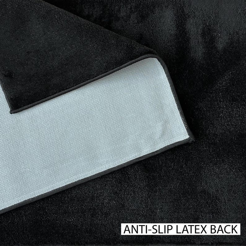 May include: Close-up of a black, textured fabric with a light gray backing. The edge of the fabric is visible, showing a black border. The text "ANTI-SLIP LATEX BACK" is printed in white at the bottom.