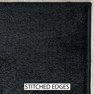 May include: Close-up of a black carpet with a textured surface. The carpet has stitched edges and a dark color. The text "STITCHED EDGES" is displayed in a white rectangle at the bottom of the image.