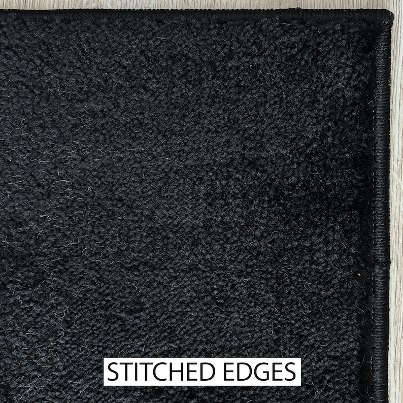 May include: Close-up of a black carpet with a textured surface. The carpet has stitched edges and a dark color. The text "STITCHED EDGES" is displayed in a white rectangle at the bottom of the image.