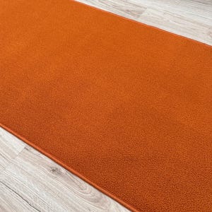 May include: A rectangular runner rug featuring a solid, vibrant orange color with a dense, textured pile surface. The rug has finished, matching orange edges and is positioned at an angle, showcasing its uniform, consistent material texture.