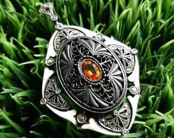 May include: A silver pendant with a black enamel center and an orange gemstone. The pendant is decorated with filigree details and small stones.