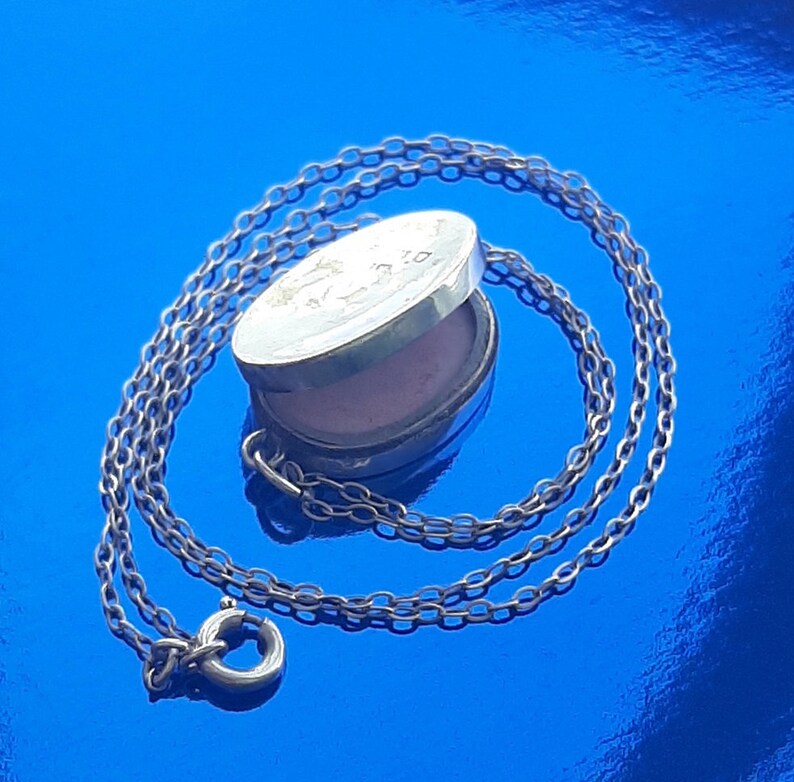 May include: A silver locket necklace with a chain. The locket is oval shaped and has a hinged lid. The locket is open and shows a pink interior.