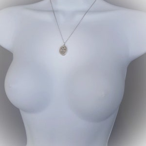 May include: A silver chain necklace with a silver oval pendant featuring a floral design.