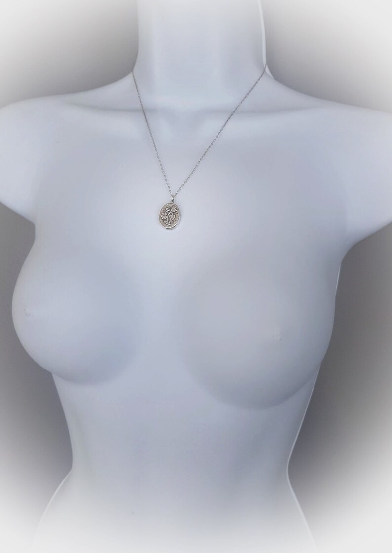 May include: A silver chain necklace with a silver oval pendant featuring a floral design.
