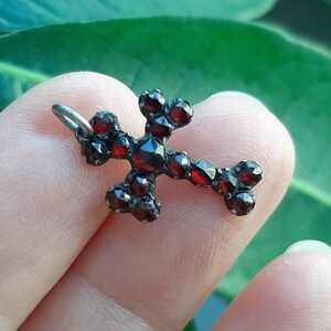 May include: A silver cross pendant set with red garnet stones.