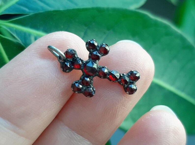 May include: A silver cross pendant set with red garnet stones.