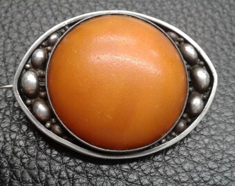 May include: Oval-shaped antique brooch with a large, smooth, amber-colored center stone. The stone is surrounded by a silver-toned metal frame with a beaded edge and decorative silver accents. A pin is attached to the back.