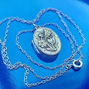 May include: A silver locket necklace featuring a floral design. The locket is oval shaped and has a delicate chain.