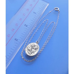 May include: A silver chain necklace with a silver oval locket featuring a floral design. The locket is approximately 2.5 cm in diameter.