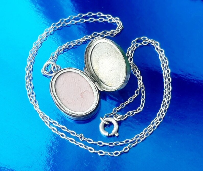 May include: A silver locket necklace with a chain. The locket is oval shaped and has a hinged lid. The locket is open and the inside is visible.