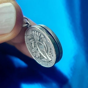 May include: Silver locket pendant featuring an engraved floral design. The locket is oval shaped and has a hinged lid.