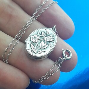 May include: A silver locket necklace featuring a floral design. The locket is oval shaped and intricately engraved with flowers and leaves. The chain is a fine silver chain.