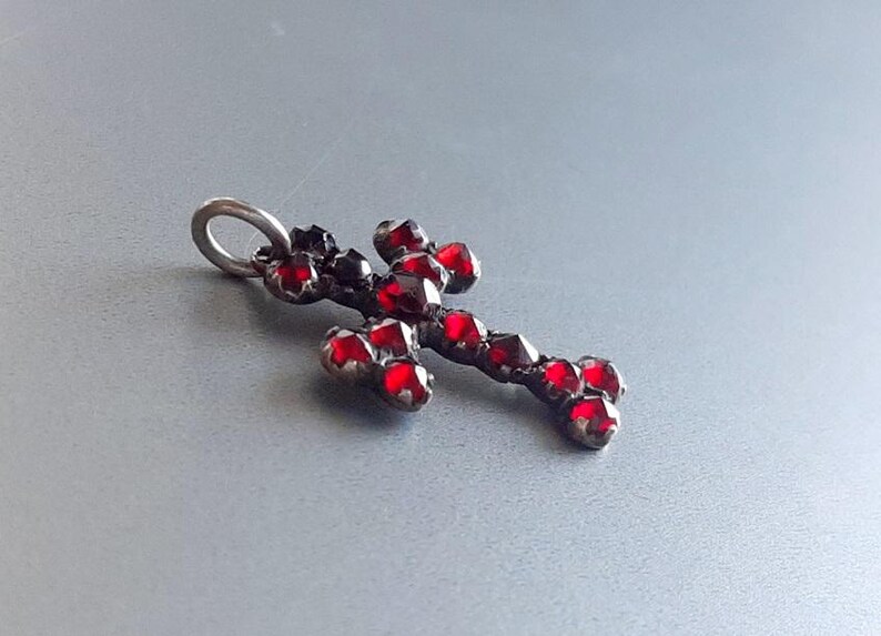 May include: A silver cross pendant with red glass stones. The cross is made of metal and has a loop at the top for hanging.
