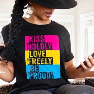 May include: A black t-shirt with the text "KISS BOLDLY LOVE FREELY BE PROUD!" in pink, yellow, and blue blocks. The text is in a distressed font style.
