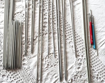 May include: A collection of silver knitting needles of various sizes, including double pointed needles and circular needles. There are also two crochet hooks, one red and one blue.