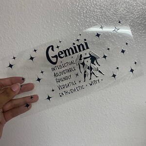 May include: A clear sticker with a black and white illustration of the Gemini zodiac sign. The sticker includes the text "Gemini", "Intellectual", "Adjustable", "Friendly", "Versatile", "Enthusiastic", and "Witty".