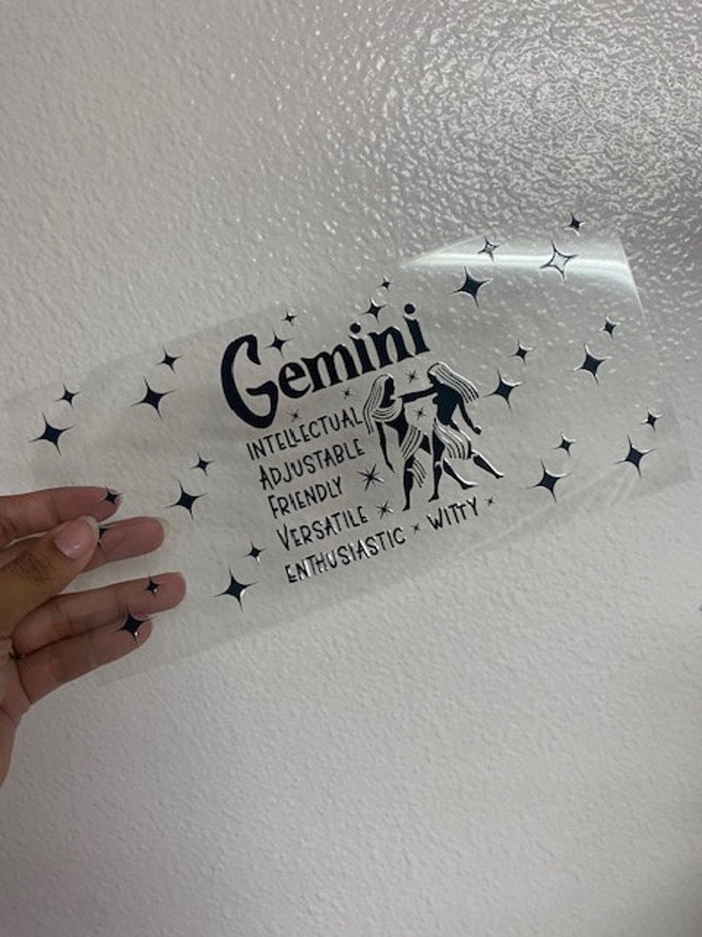May include: A clear sticker with a black and white illustration of the Gemini zodiac sign. The sticker includes the text "Gemini", "Intellectual", "Adjustable", "Friendly", "Versatile", "Enthusiastic", and "Witty".