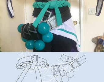May include: A cosplay belt and accessory set featuring a black waistband with silver buckles, a teal braided fabric sash, and a black pouch adorned with multiple glossy teal spheres. The image includes a line art diagram labeled PDF PATTERN.