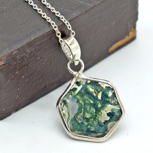 Op de afbeelding: Een zilveren ketting met een zeshoekige hanger met een groene en witte mosagaat.