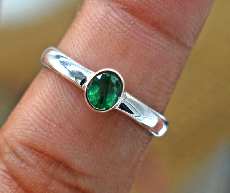 May include: A silver ring with a green gemstone. The ring is on a finger.