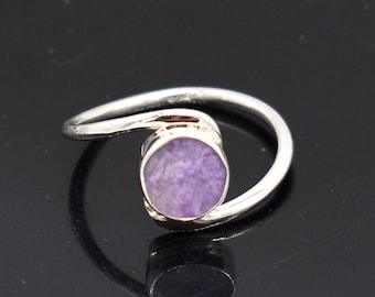 May include: A silver ring with a purple stone set in a bezel setting. The ring has a unique, curved band.