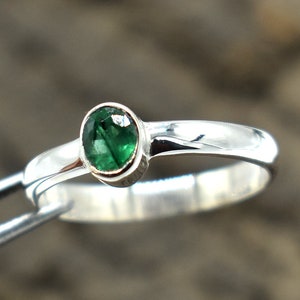 May include: A silver ring with a green gemstone set in a bezel setting.