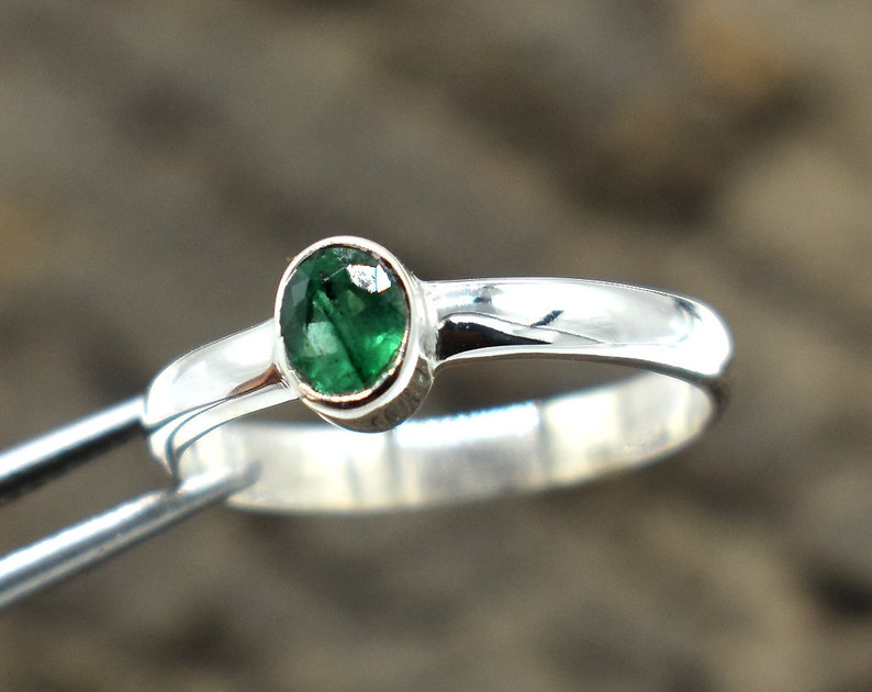 May include: A silver ring with a green gemstone set in a bezel setting.
