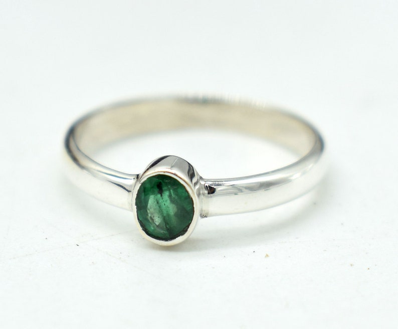 May include: A silver ring with a green emerald gemstone.