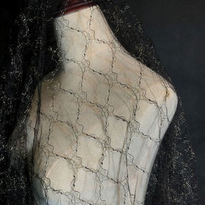 May include: Black sheer fabric with a gold metallic pattern. The fabric has a delicate, lacy texture.