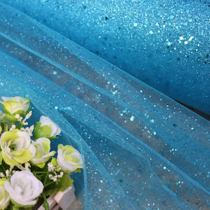 Può includere: Tessuto di tulle blu turchese con glitter iridescente. Il tessuto è trasparente e ha una texture delicata.