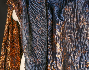 May include: A close-up of a fabric with a metallic sheen. The fabric has a wavy pattern and is a combination of blue and gold colors.