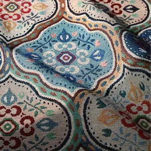 May include: Close-up of a colourful fabric with a repeating pattern of blue, green, red, and yellow geometric shapes. The fabric has a textured woven look.