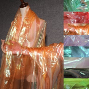 Op de afbeelding: Een verzameling van iriserende, doorschijnende stoffen in verschillende kleuren, waaronder groen, roze, paars, blauw, grijs, zwart en limoengroen. De stoffen zijn doorschijnend en glinsterend, met een subtiele glans.