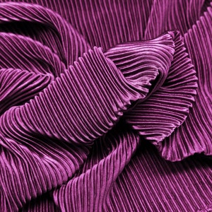 May include: Close-up of a deep purple pleated fabric. The fabric is folded and draped, showing the texture and folds of the material.