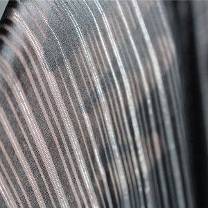 Puede incluir: Primer plano de una tela negra con rayas plateadas. La tela tiene un brillo sutil y una textura suave y fluida.