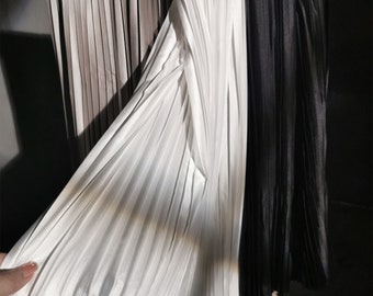 May include: A white pleated skirt with a black pleated skirt behind it. The skirts are made of a silky material and are hanging on a rack.