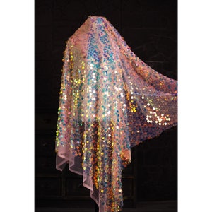 Puede incluir: Una tela rosa transparente con lentejuelas iridiscentes en forma de cuadrado. La tela está drapeada sobre un maniquí.