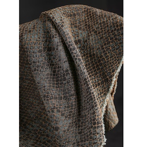 May include: A close-up shot of fabric with a snakeskin pattern. The material is a blend of brown, black, and teal hues. The texture is evident, featuring a scale-like design. The fabric is draped, highlighting its flexibility and texture.