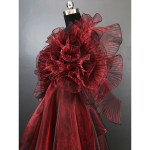 Può includere: Un abito di tulle bordeaux con un grande design floreale a balze sulla spalla.